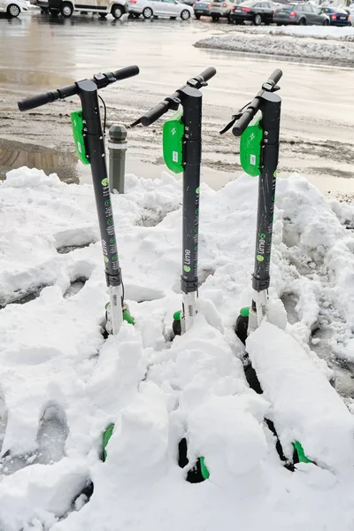 Tres scooters eléctricos Lime estacionados y cubiertos con una capa fresca de nieve, durante una temporada de invierno suave en Bucarest, Rumania . —  Fotos de Stock