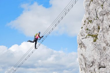 Avusturya 'daki Intersport Klettersteig Donnerkogel adlı ferrata rotasında ayağını kaldıran kadın turist. Cennete giden merdiven kavramı.
