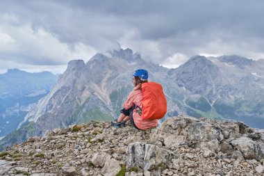 Colac tepesindeki kadın, Ferrata dei Finanzieri 'nin sonunda, kaskını takmış ve yağmur örtülü bir sırt çantasıyla panoramik manzaranın tadını çıkarıyor, fırtına bulutları yaklaşıyor..