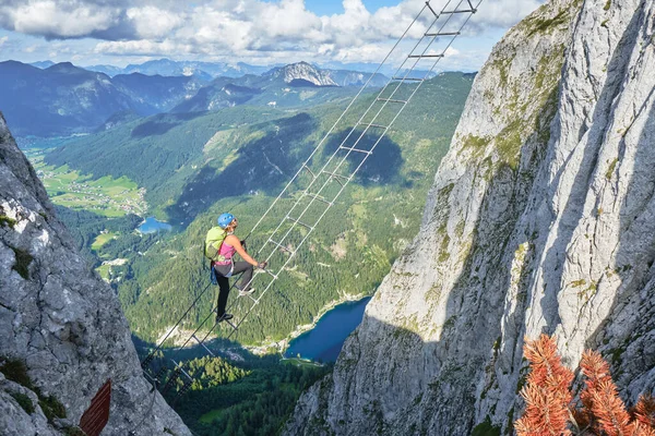 Avusturya 'daki Intersport Klettersteig Donnerkogel rotasında Gosau Gölü' nün yukarısındaki Ferrata merdiveninde bir kadın. Bir yaz gününde yüksek açı görünümü.