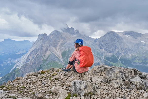 Colac tepesindeki kadın, Ferrata dei Finanzieri 'nin sonunda, kaskını takmış ve yağmur örtülü bir sırt çantasıyla panoramik manzaranın tadını çıkarıyor, fırtına bulutları yaklaşıyor..