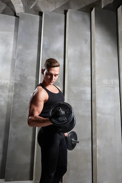 man in black sports uniform with dumbbells on a background of gray wall