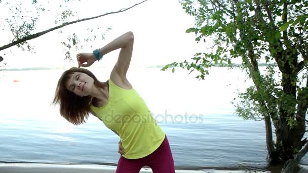 Joven mujer haciendo estiramiento cerca del río — Vídeos de Stock