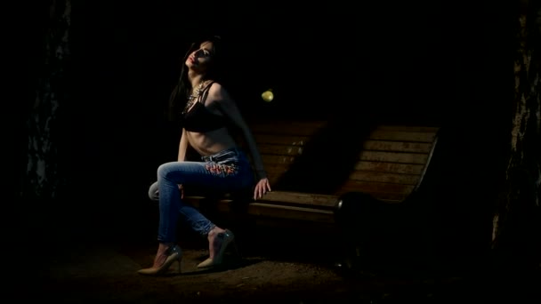 Sexy brunette girl sits on a bench at night — Stock Video