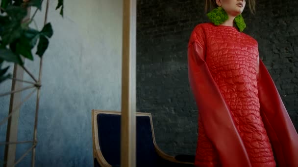Model mode meisje in rode kleding en make-up zit neer in een donker blauwe leunstoel — Stockvideo