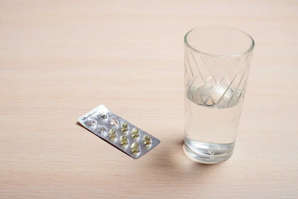Bolha com pílulas e um copo de água em uma mesa brilhante — Fotografia de Stock