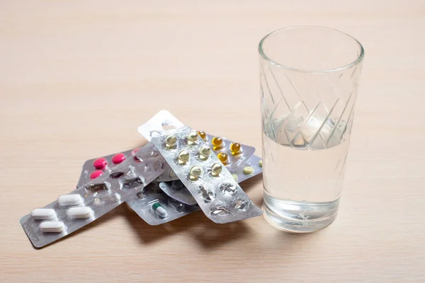 Blister con pillole e un bicchiere d'acqua poggiano su un tavolo luminoso — Foto Stock