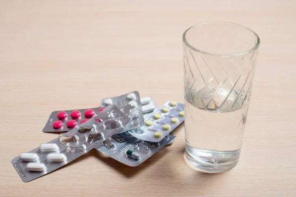 Blister con pillole e un bicchiere d'acqua poggiano su un tavolo luminoso — Foto Stock