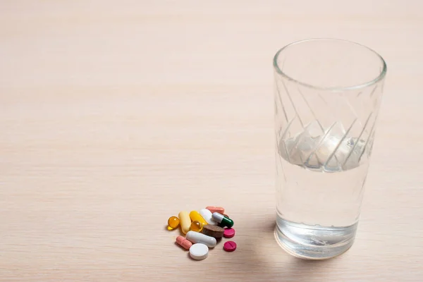 Pillole multicolori e un bicchiere d'acqua poggiano su un tavolo leggero — Foto Stock