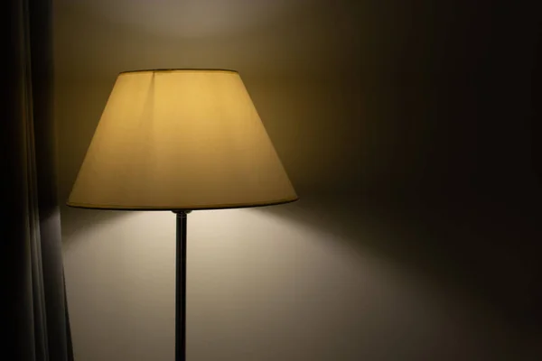 A yellow floor lamp against a white wall in a dimly lit room.