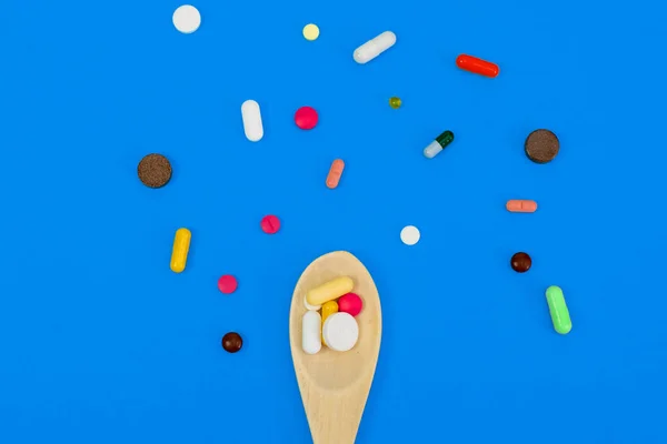 Multi-colored pills in a wooden box around her. Copyspace on a blue background. Medical concept — Stock Photo, Image