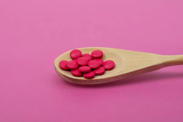 Pillole rosa in un cucchiaio di legno su sfondo rosa. Primo piano — Foto Stock