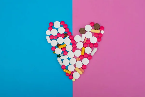 Cuore fatto di pillole multicolori su uno sfondo rosa e blu. Copia spazio per testo — Foto Stock