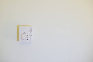 Beyaz bir odada beyaz bir termostat asılı.