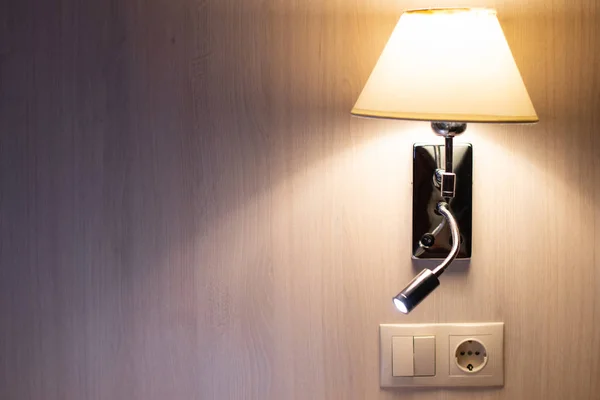 Double bedside lamp that casts light and shadow on the wall.