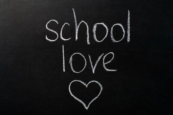 A inscrição "amor escolar" em um quadro negro com giz branco. Imagem do coração — Fotografia de Stock