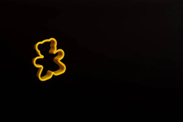 黒い背景にテディベアの形でクッキーを作るための黄色のプラスチック製のクッキーカッター 料理のコンセプト コピースペース付きのフラットレイアウト — ストック写真