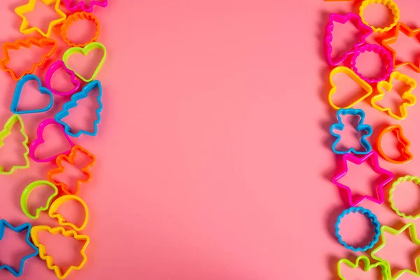 Multi-colored plastic molds of various shapes grouped on the right and left for making cookies on a pink background. Culinary concept. Flat lay with copyspace.