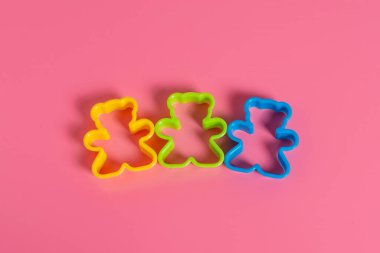 Pembe arka planda oyuncak ayı şeklinde kurabiye yapmak için üç adet mavi, sarı ve yeşil renkli plastik kalıp. Mutfak konsepti. Kopyalama alanı ile düz uzandı.