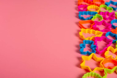 Sağda, pembe arka planda kurabiye yapmak için gruplandırılmış çeşitli şekillerdeki çok renkli plastik kalıplar. Mutfak konsepti. Kopyalama alanı ile düz uzandı.