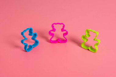 Pembe arka planda oyuncak ayı şeklinde kurabiye yapmak için üç adet mavi, pembe ve yeşil renkli plastik kalıp. Mutfak konsepti. Kopyalama alanı ile düz uzandı.