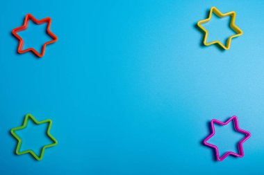 Mavi arka planda yıldız şeklinde kurabiye yapmak için dört renkli plastik kurabiye kesicisi. Mutfak konsepti. Kopyalama alanı ile düz uzandı.