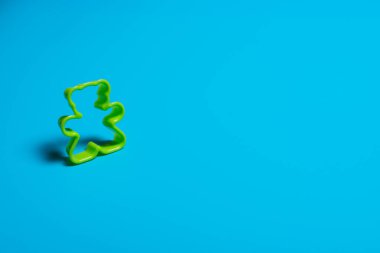 Mavi arka planda oyuncak ayı şeklinde kurabiye yapmak için yeşil plastik kurabiye makası. Mutfak konsepti. Kopyalama alanı ile düz uzandı.