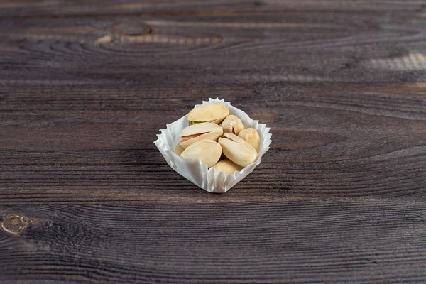 A serving of pistachios in a paper muffin cup on a dark wood background.