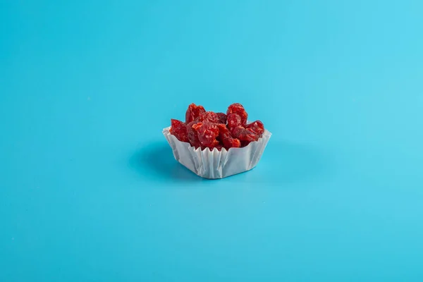 A serving of dried cherries in a paper muffin cup on a blue background.