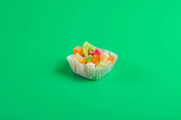 緑の背景に紙マフィンカップに砂糖漬けの果物の一部 — ストック写真