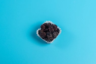 Mavi arka planda kağıttan bir kek fincanında siyah üzümler..