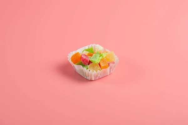 ピンクの背景に紙のマフィンカップに砂糖漬けの果物の一部 — ストック写真