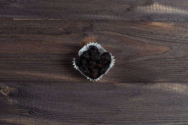 A portion of black raisins in a paper muffin cup on a dark wood background.