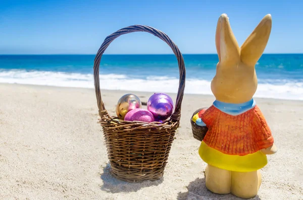 Великодній кролик з кошиком і кольоровими яйцями на тропічному пляжі — стокове фото