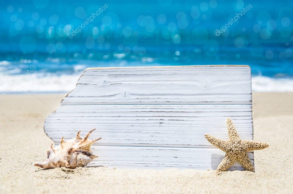 White wood board with seashell  and starfish on the sandy beach