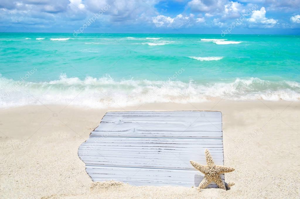White wood board with starfish on the sandy beach