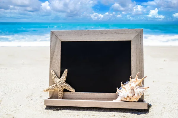 Pizarra de madera negra con concha marina y estrella de mar en la arena b —  Fotos de Stock