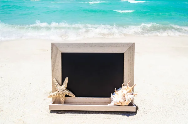 Lavagna in legno nero con conchiglia e stelle marine sulla sabbia essere — Foto Stock