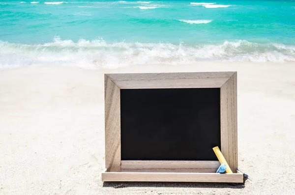 Pizarra de madera negra con tiza en la playa de arena —  Fotos de Stock