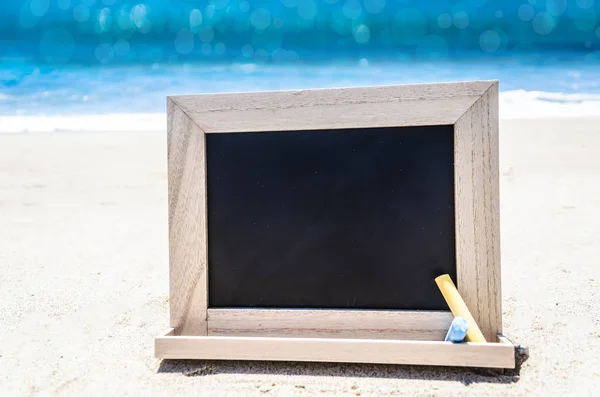 Pizarra de madera negra con tiza en la playa de arena —  Fotos de Stock