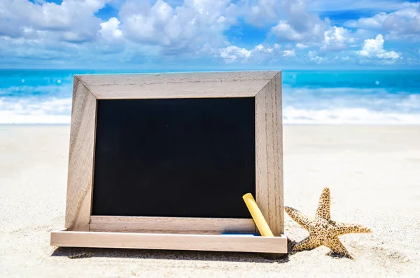 Zwarte houten schoolbord met zeester en krijt aan het zandstrand — Stockfoto