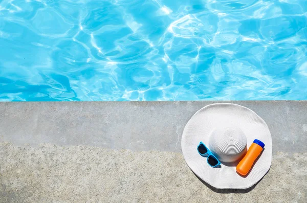 Sombrero de verano, gafas de sol y protector solar cerca de la piscina — Foto de Stock