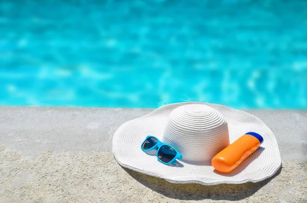 Chapéu de verão, óculos de sol e protetor solar perto da piscina — Fotografia de Stock