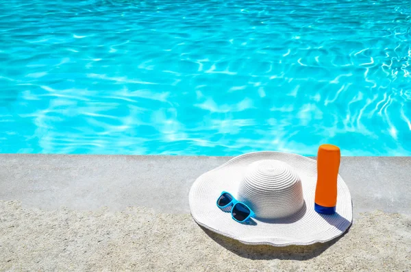 Летняя шляпа, солнцезащитные очки и солнцезащитный крем у бассейна — стоковое фото