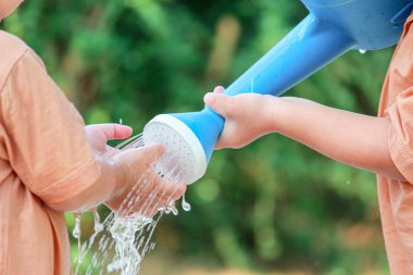 Asyalı kız ve kız kardeşi mavi sulama kutusundan su oynarken eğleniyorlar..