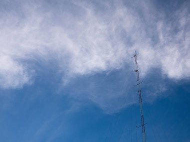 Tv ve radyo direği telekomünikasyon antenleri bulutlarda ve mavi gökyüzü arka planında.