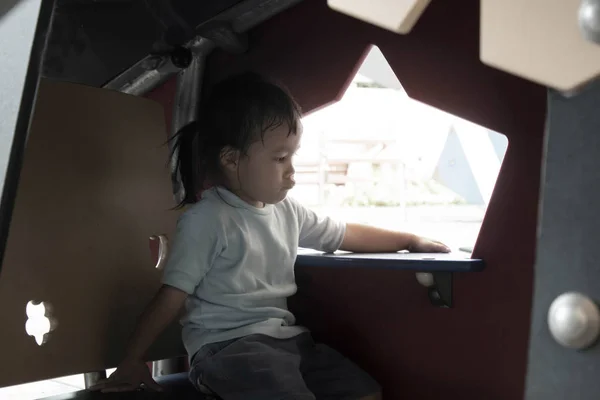 Asiatisches kleines Mädchen sitzt zum Ausruhen in kleinem Plastikhaus auf dem Spielplatz. — Stockfoto