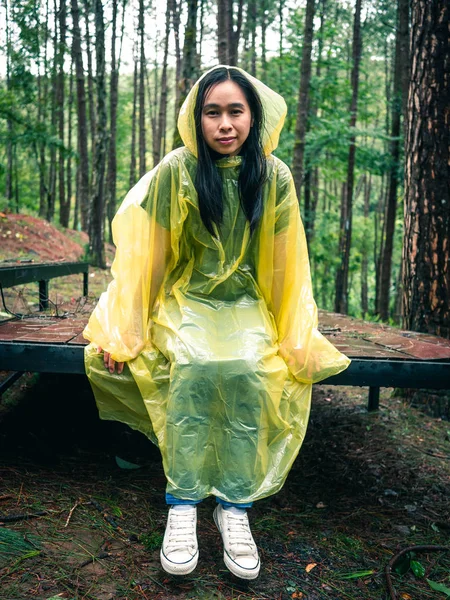Ευτυχισμένη Ασιάτισσα που φοράει κίτρινο αδιάβροχο καθισμένη σε ξύλινο ελάφι — Φωτογραφία Αρχείου