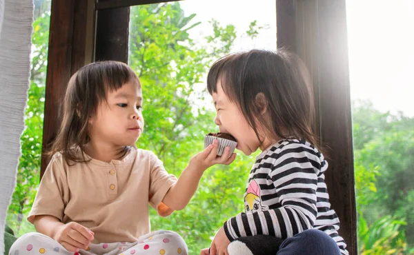 Ασιατικό κοριτσάκι και η αδερφή της τρώνε κεκάκια μπανάνας στο δωμάτιο υπέροχα.. — Φωτογραφία Αρχείου
