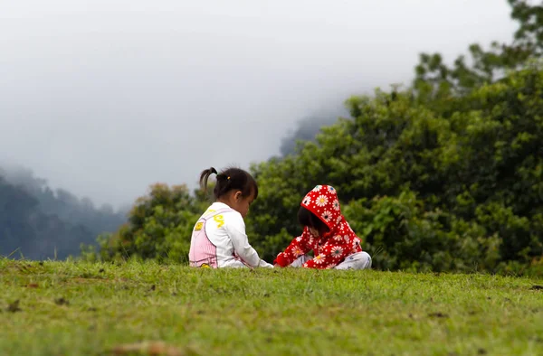 Malé asijské děvčátko pomáhalo obout sestru v trávě na hoře Ang Khang, Fang Chiang Mai. Turistické atrakce na severu Thajska. — Stock fotografie